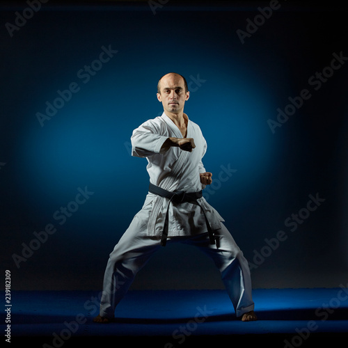 A man does formal karate exercises on a blue tatami
