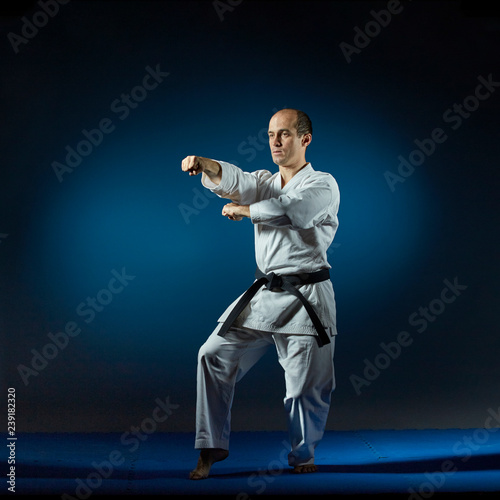 A man performs formal karate exercises on a blue tatami
