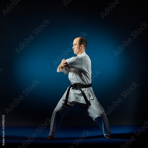 A man trains formal karate exercises on a blue tatami