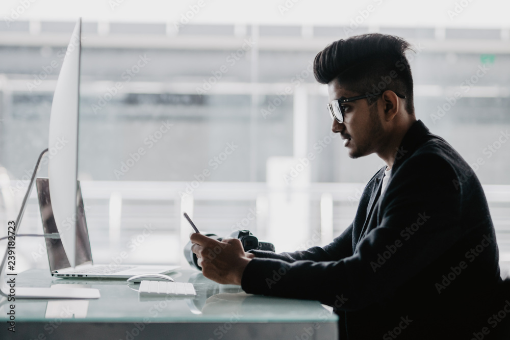 handsome young man retouching photos at workplace while use phone in office handsome young man retouching photos at workplace while use phone in office