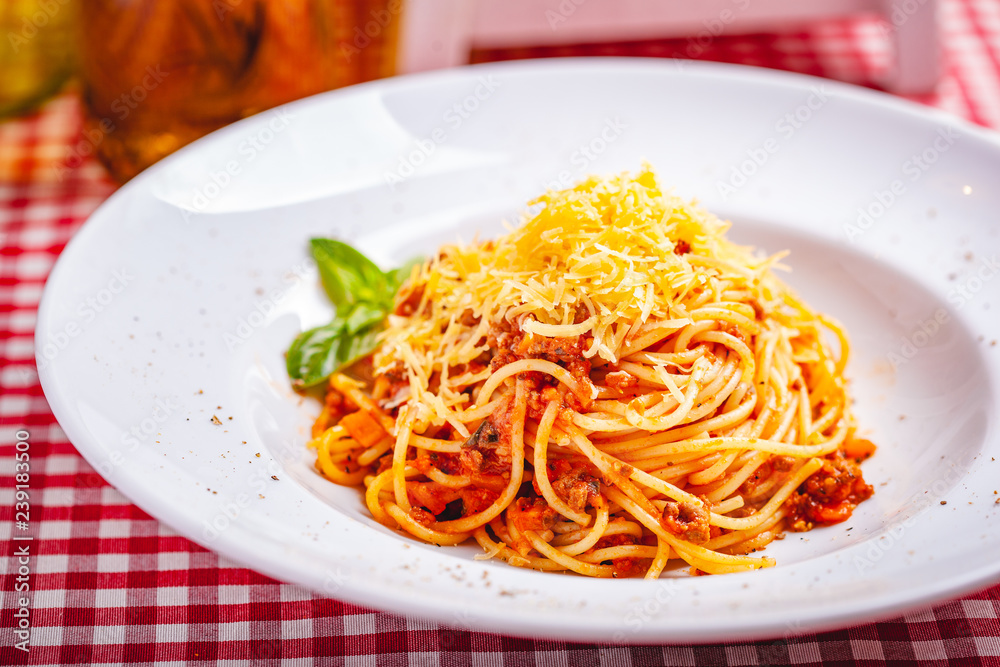 Italian cuisine. Spaghetti bolognese with meat, parmesan cheese and tomatoes on white plate. Close up