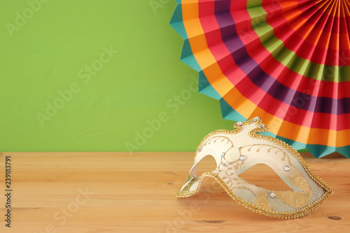 carnival party celebration concept with elegant gold mask over wooden table and green background background.