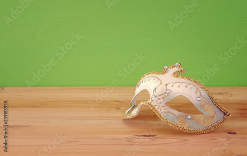 carnival party celebration concept with elegant gold mask over wooden table and green background background.