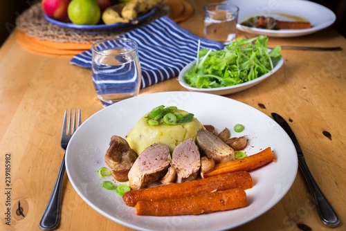 Pork tenderloin,mashed potato and carrot on plate, salad on wooden table.