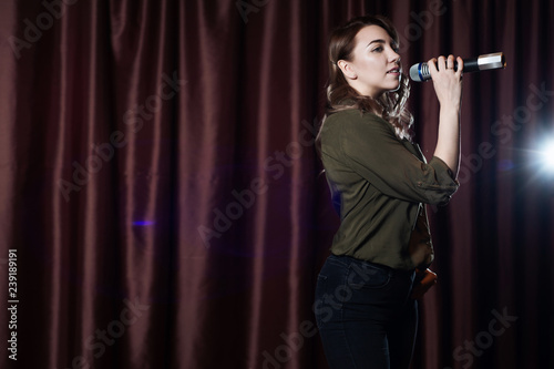 Woman singing on stage in the microphone karaoke on the background of red curtains