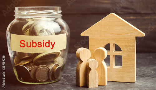 The family is standing near a glass jar with the inscription Subsidy. Financial aid, support to the population. Cash grants, interest-free loans. Tax breaks, insurance, low-interest loans