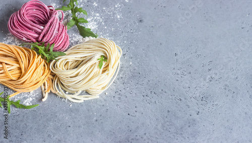 Variety of colored fresh uncooked homemade pasta noodle with flour over grey slate, stone or concrete table. Top view. Food background. Copy space for text.