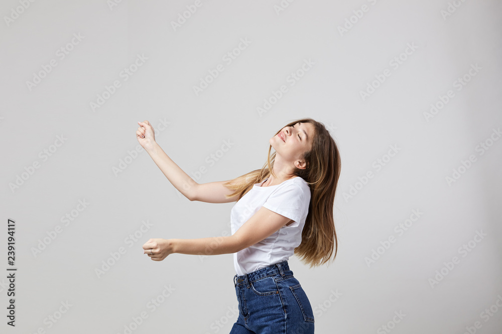 Cheerful and calm girl dressed in a white t-shirt and jeans has fun on a white background in the studio Cheerful and calm girl dressed in a white t-shirt and jeans has fun on a white background in the studio