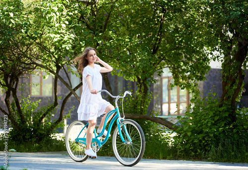 Long haired young woman in a dress riding bicycle in the bark copyspace emotions freedom freshness weekend hobby active living.