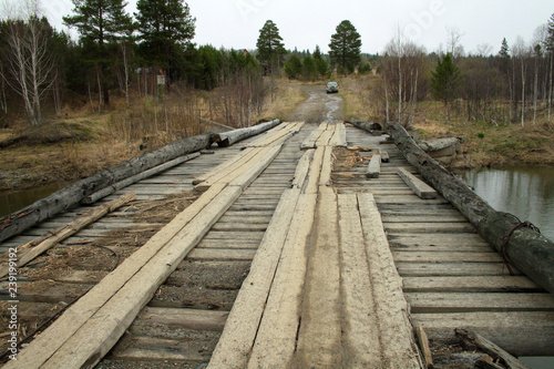 wide wooden bridge of planks over the river and forest road with a car © taushka