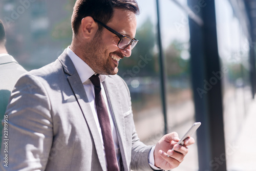 Close up of smiling businessman dressed in formal wear using smart phone for reading or writing message.