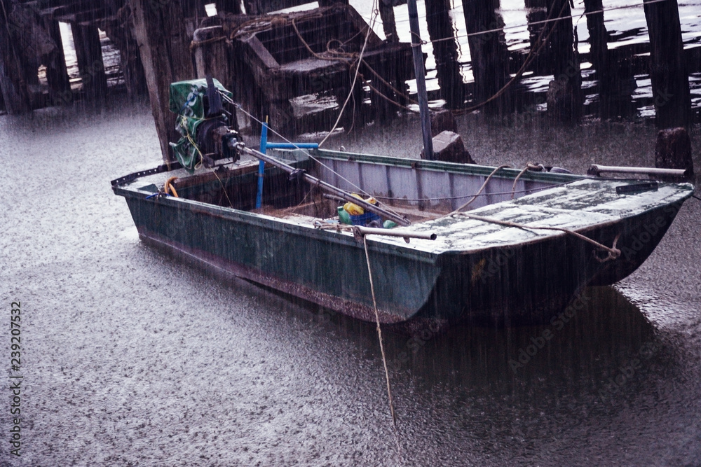 Old single motor boat in heavy rain at a port in Thailand.