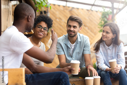 African American man showing thumb up, telling story to interested attentive friends, sitting, drinking coffee in cafe together, smiling multiethnic friends discussing, talking, chatting