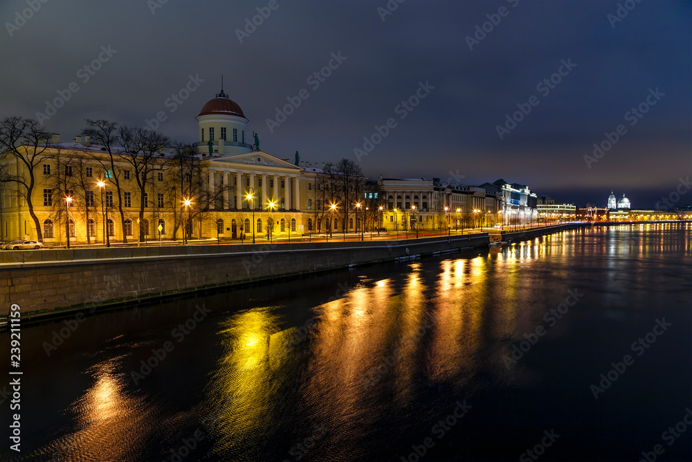 Neva river embankment with historical buildings on the shore and reflection of night lights in the water, beautiful sunset sky. Petersburg, Russia
