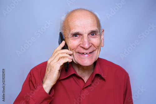 portrait of a senior elderly man in a red shirt, cheerful laughs talking on the phone