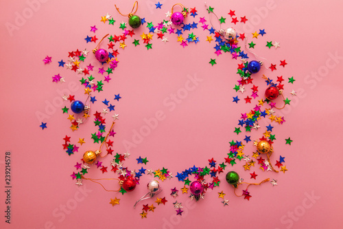 Pink christmas background with frame made of multicolor christmas balls and bright star confetti. Chistmas and new year concept.