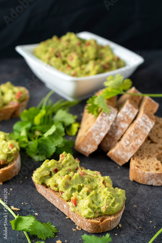Fresh bread with Mexican homemade guacamole on a black table.