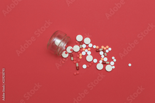 Pills scattered from a flask on a red background