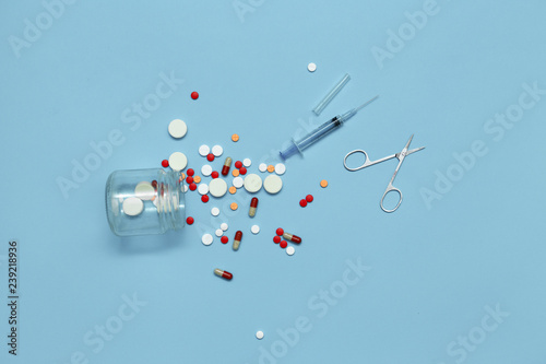 A scattering of pills, medical syringe and scissors on a blue background