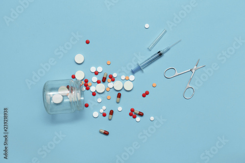Scattering of pills, syringe and scissors on a blue background