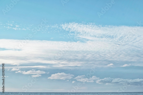 Cumulus and cirrocumulus clouds in the clear bright blue sky in the afternoon on the sea coast with a small strip of the sea below