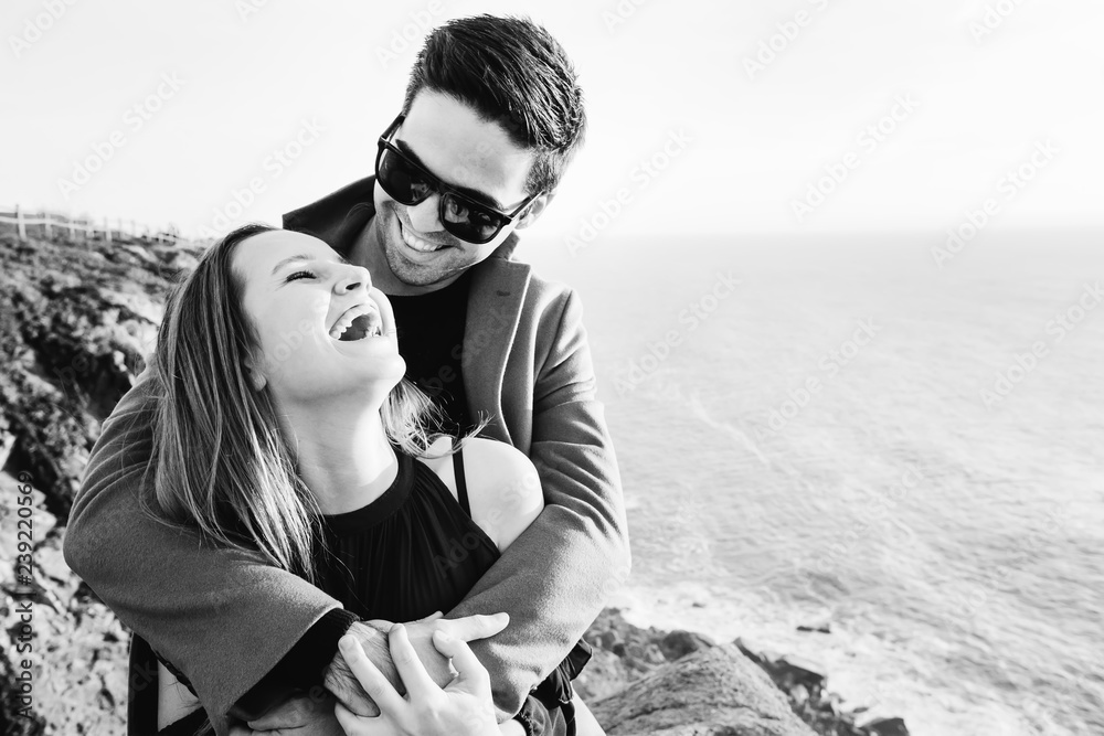 a guy in a coat and sunglasses hugs a girl who sincerely laughs