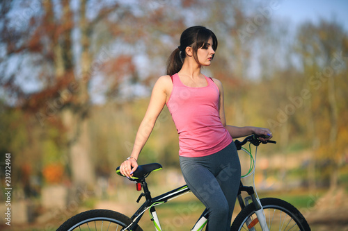 Young beautiful girl in sportswear stands next to a bicycle on the street in the park in autumn.