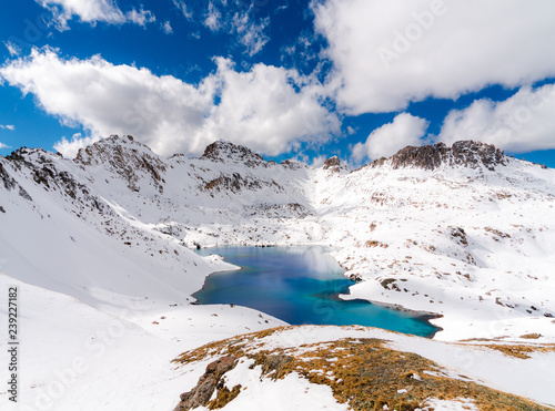 A very deep blue lake sits in a valley between snow capped mountains on a partly cloudy day