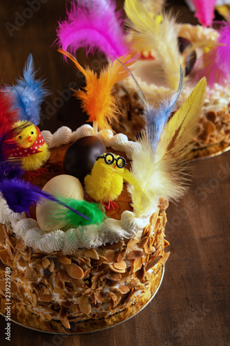 Fotografi Closeup of a mona de pascua, a cake eaten in Spain on Easter Monday, ornamented with feathers and a teddy chick on on a rustic wooden surface