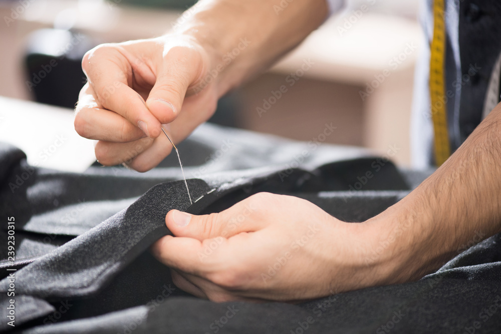 Obraz premium Closeup of unrecognizable male tailor sewing classic jacket in traditional atelier studio, copy space