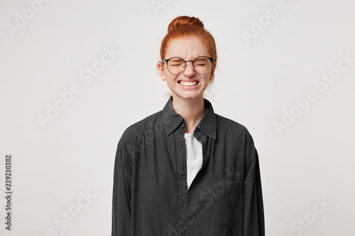 Red-haired girl student wearing glasses, eyes closed, face grimace as if she forgot to do something necessary, now she remembered something important, deeply regrets that she didn't make in time