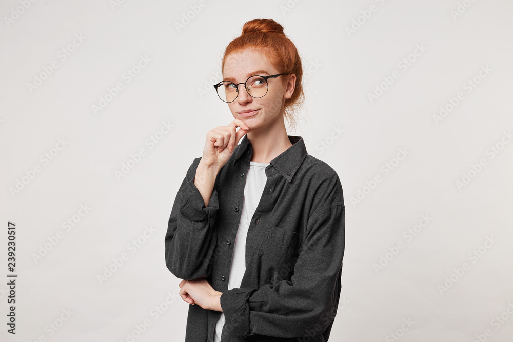 Portrait of young red -hair female in black men's shirt, keeps arm on chin and looks up, ponders the idea, consider different variants, thinking what do to solve the problem, over white background Portrait of young red -hair female in black men's shirt, keeps arm on chin and looks up, ponders the idea, consider different variants, thinking what do to solve the problem, over white background