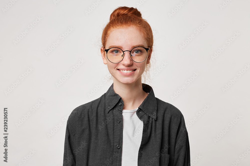 A smiling cheerful happy young girl in glasses with red hair looks straight into the camera isolated on a white background.