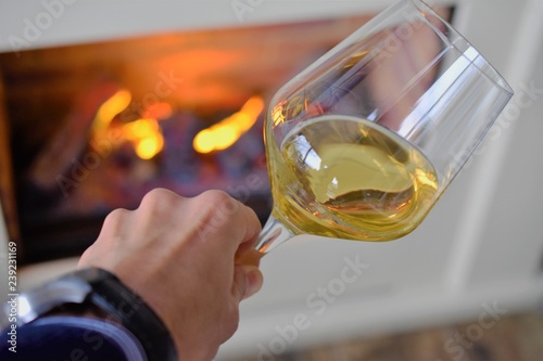 hand with glass of white wine, wine tasting in the restaurant next to the fireplace