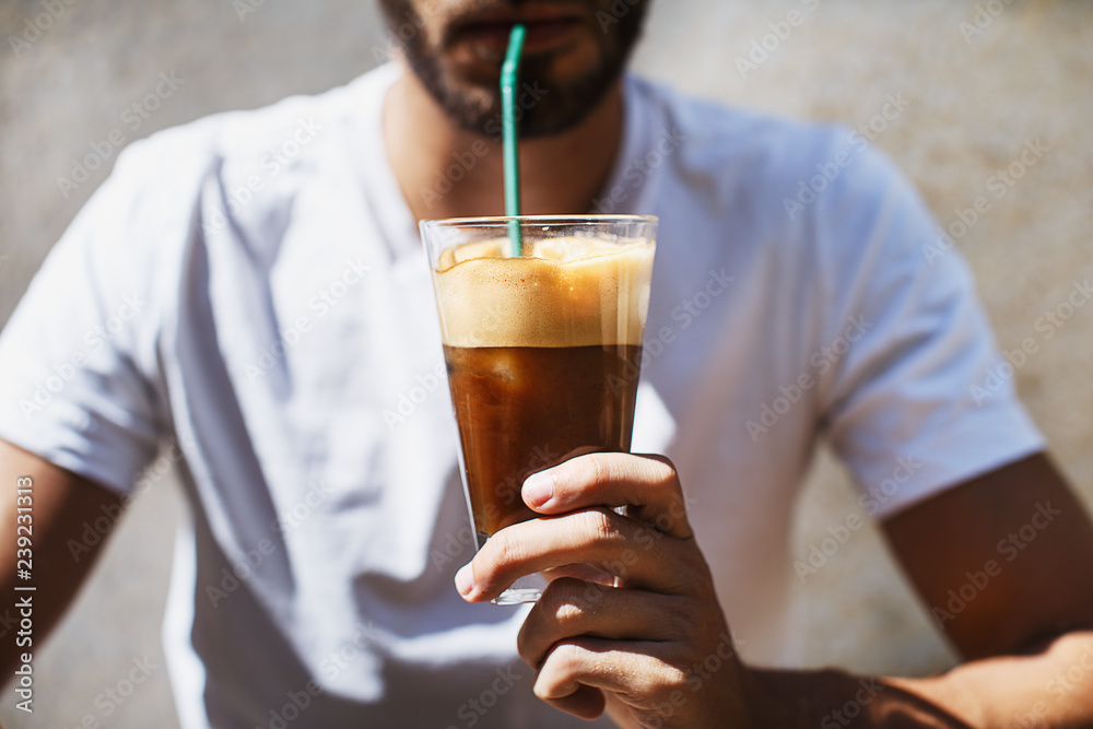 A man is drinking an ice coffee on a sunny day, taken from a front view A man is drinking an ice coffee on a sunny day, taken from a front view