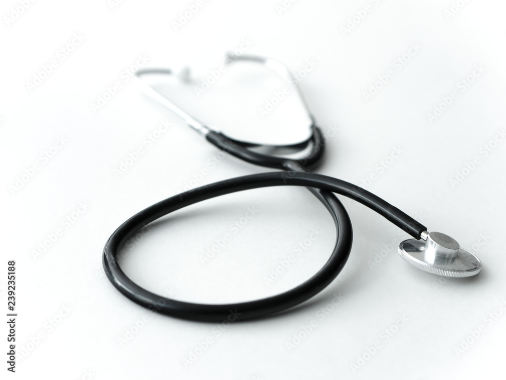 A doctors black flexible rubber and steel metal heart pulse stethoscope laying isolated on a white table top. A doctors black flexible rubber and steel metal heart pulse stethoscope laying isolated on a white table top.