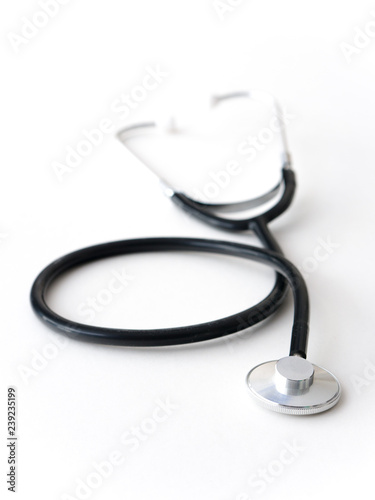 A doctors black flexible rubber and steel metal heart pulse stethoscope laying isolated on a white table top.