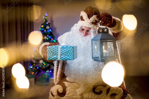 Santa Claus with a candle lantern looking at gifts. Santa brings and distributes gifts.