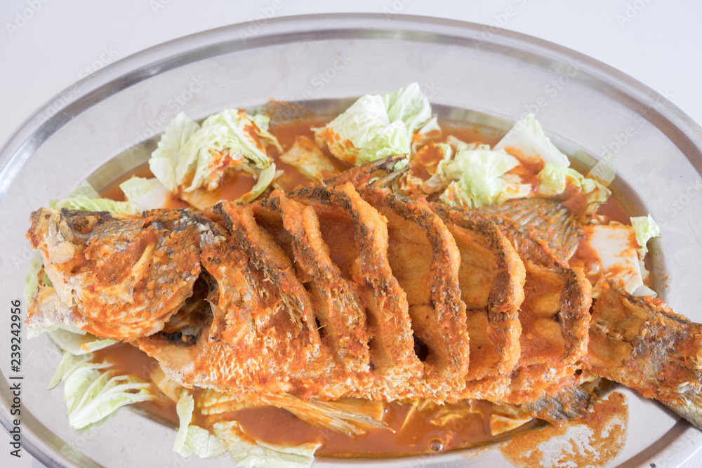 Thai dinner food fried barramundi fish with herb on the white plate over white table in restaurant