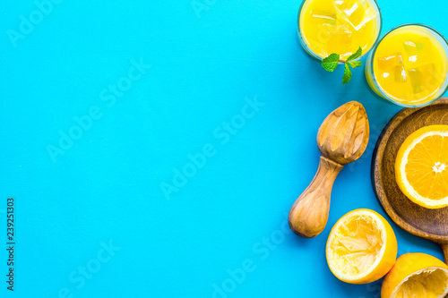 Make orange juice. Juice in glass near half cut oranges and jucier on blue background top view copy space