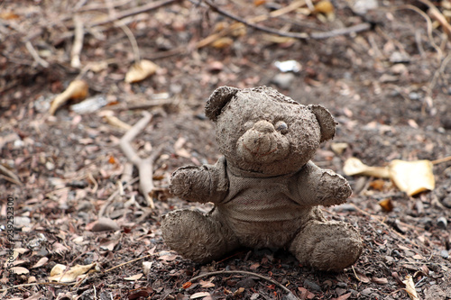 Old dirty teddy bear neglected on the ground soil. End of childhood.