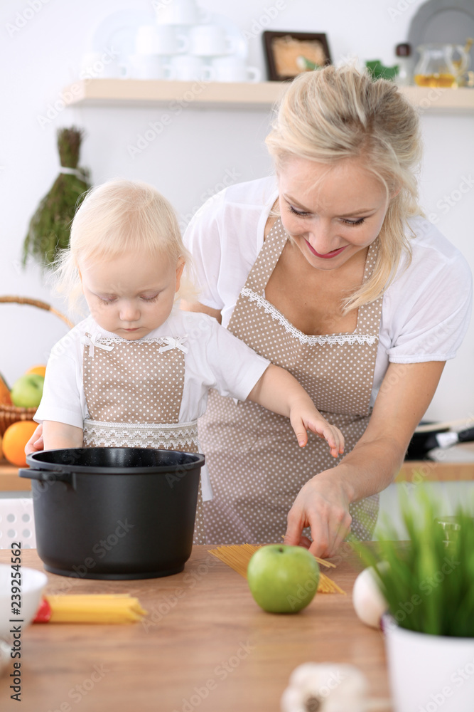 Happy mother and little daughter cooking in kitchen. Spending time all together, family fun concept