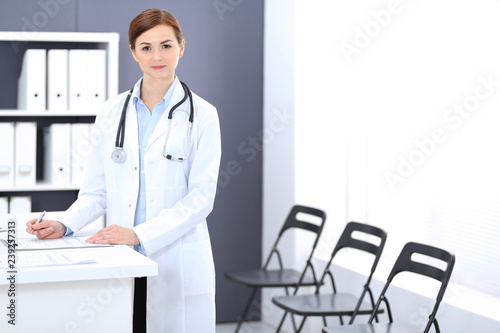 Doctor woman at work. Portrait of female physician filling up medical form while standing near reception desk at clinic or emergency hospital. Medicine concept