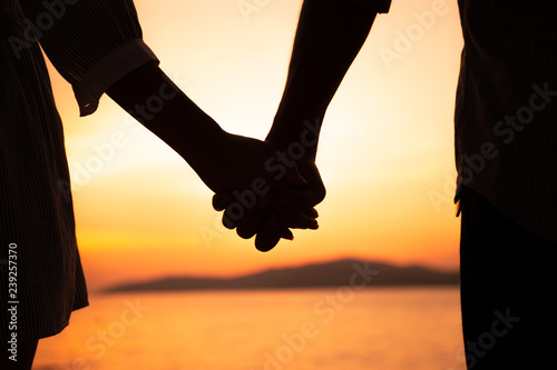 Couple hold hands in summer time on sunset at beach