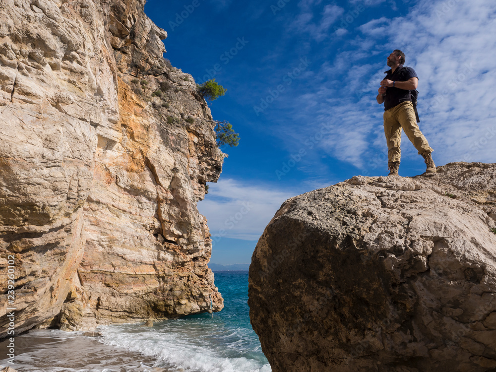 Traveler with backpack on the rocks near the sea looking away. Summer Travel Vacation. Handsome young caucasian tourist man in casual clothes outdoors on the nature