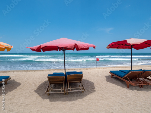 Red sun umbrellas stay on white sand beach with blue sea and blue sky on background. Concept for rest, relaxation, holidays, spa, resort. Bali, Indonesia, october 2018