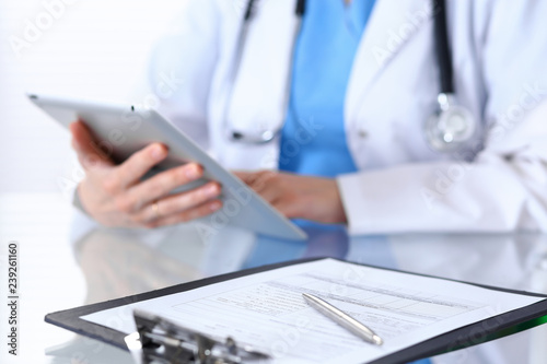 Woman doctor using tablet computer while sitting at the desk in hospital office, closeup. Healthcare, insurance and medicine concept