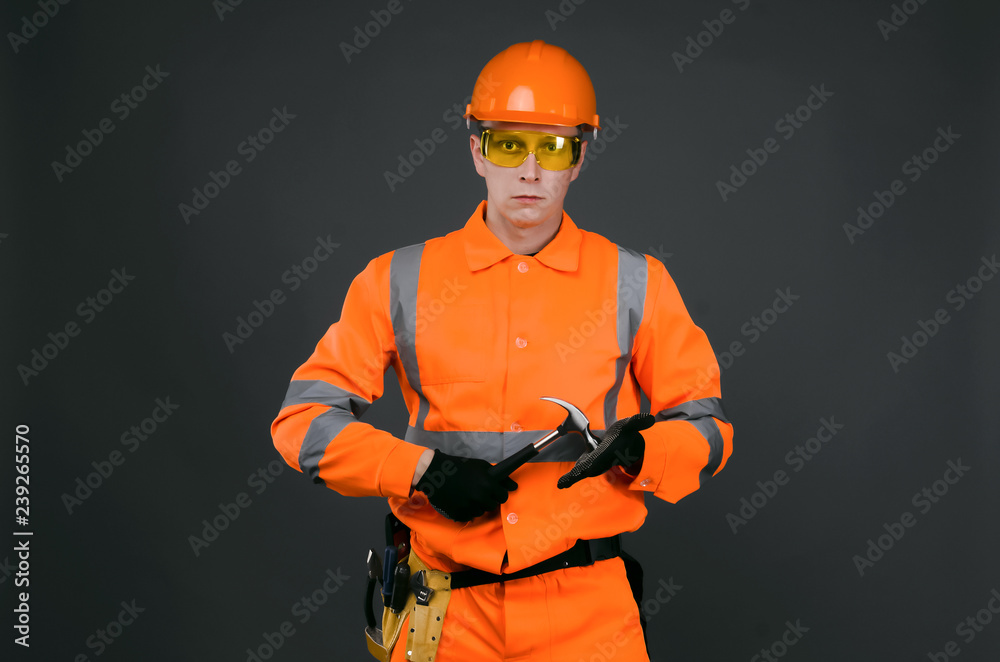 Serious builder construction worker holding a hammer in his hands. Under construction. Serious builder construction worker holding a hammer in his hands. Under construction.