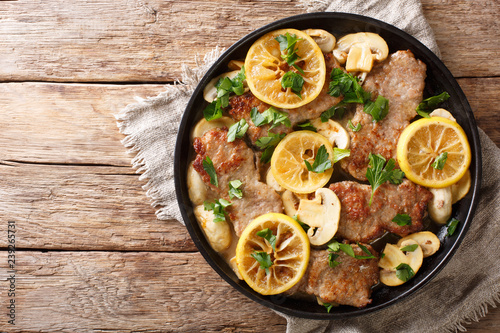 Tasty Italian fillet of veal scaloppini with mushrooms and lemons in sauce close-up in a frying pan. Horizontal top view photo