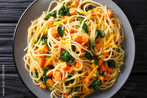 Low-calorie lunch of spaghetti with pumpkin, spinach and cheddar cheese close-up on a plate. horizontal top view